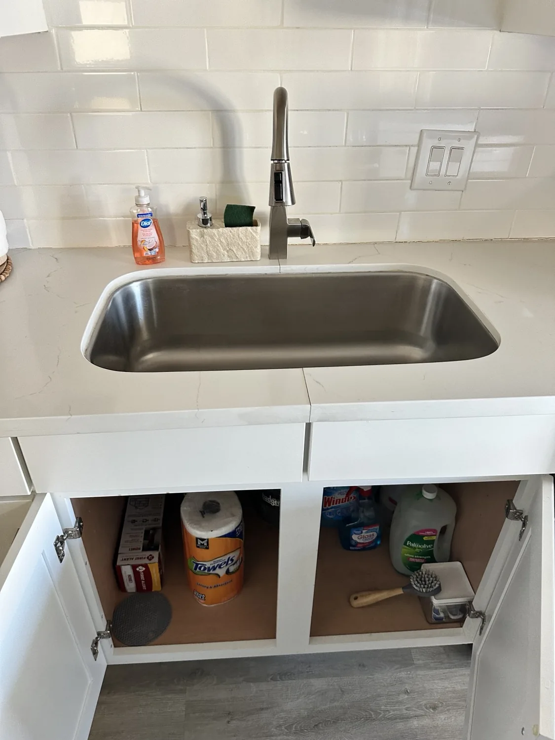 Kitchen sink and open cabinet showing stored cleaning supplies